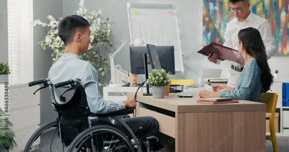 A man sits in a wheelchair at a desk in an office, across from him a beautiful woman in a dress, they sign a cooperative employment agreement, thank each other for interview, congratulate A man sits in a wheelchair at a desk in an office, across from him a beautiful woman in a dress, they sign a cooperative employment agreement, thank each other for interview, congratulate