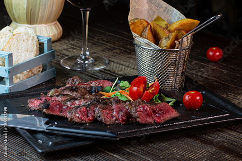 Tagliata di manzo con patate al forno servita in un piatto di ghisa quadrato.  photo