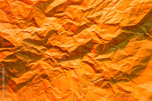 Photo of crumpled wrinkled orange office paper lit with red light, background texture