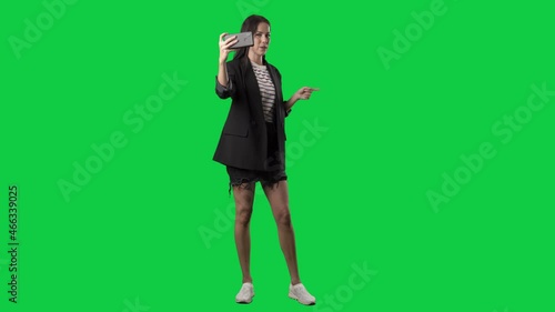 Stylish young woman social media influencer filming selfie video greeting followers. Full body isolated on green screen background