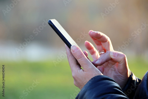 Female hands with smartphone close up on blurred city background. Woman using mobile phone outdoors, concept of sms, online addiction