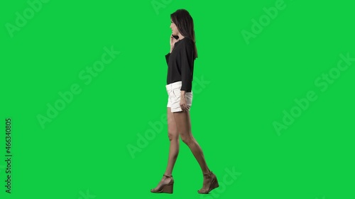 Side view of elegant young woman walking and talking on cellphone. Full body isolated on green screen background