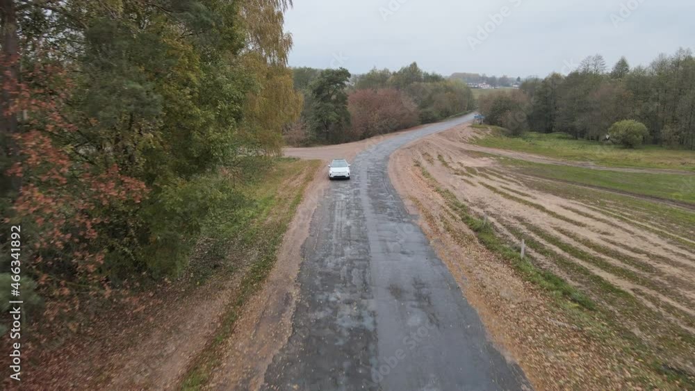 Aerial view of white electric car driving on countryside road. Modern vehicle passing rural highway. Ecology friendly car riding on electric charge along motorway. Top view Aerial view of white electric car driving on countryside road. Modern vehicle passing rural highway. Ecology friendly car riding on electric charge along motorway. Top view