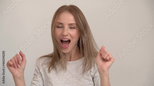 Beautiful caucasian girl dancing in front of the camera and listening music with closed eyes and dancing actively. Young woman posing on a white wall background