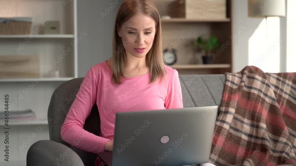 Waist up portrait view of ginger woman with happy cheery smile sitting at the sofa and working at the laptop indoors Waist up portrait view of ginger woman with happy cheery smile sitting at the sofa and working at the laptop indoors