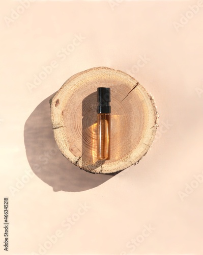 Glass perfume sample with brown liquid on a wooden tray lying on a beige background. Luxury and natural cosmetics presentation. Tester on a woodcut in the sunlight. Top view