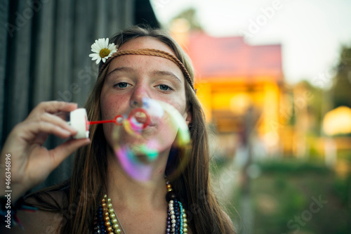 A girl In hippie clothes blows soap bubbles outdoor in the village.
