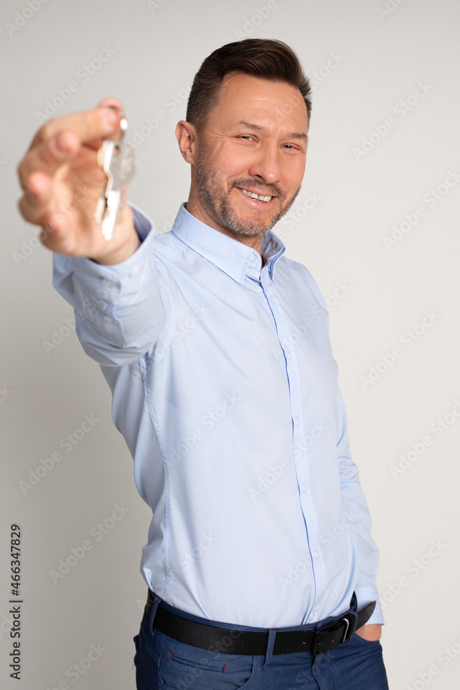 Vertical Photo of employee manager, blue shirt, of real estate agency holds in hand keys to appartments. Buying or renting house. man is happy to become home owner. Studio shot on neutral background. Vertical Photo of employee manager, blue shirt, of real estate agency holds in hand keys to appartments. Buying or renting house. man is happy to become home owner. Studio shot on neutral background.