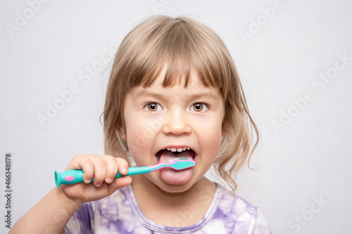 A little girl cleans her tongue and teeth with a toothbrush. Oral hygiene.