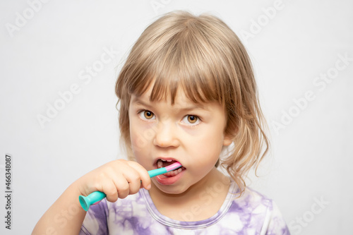 A little girl brushes her teeth with a toothbrush for children on a light background, close-up. Oral hygiene.