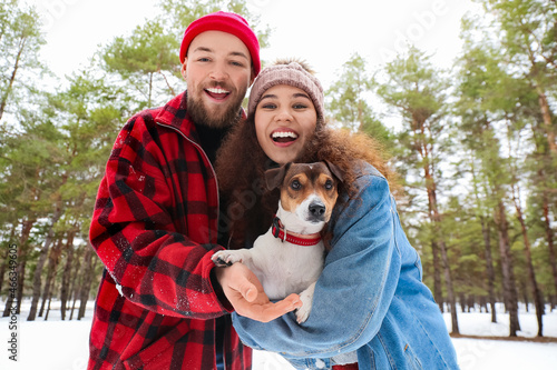 Happy young couple with dog in forest on winter day