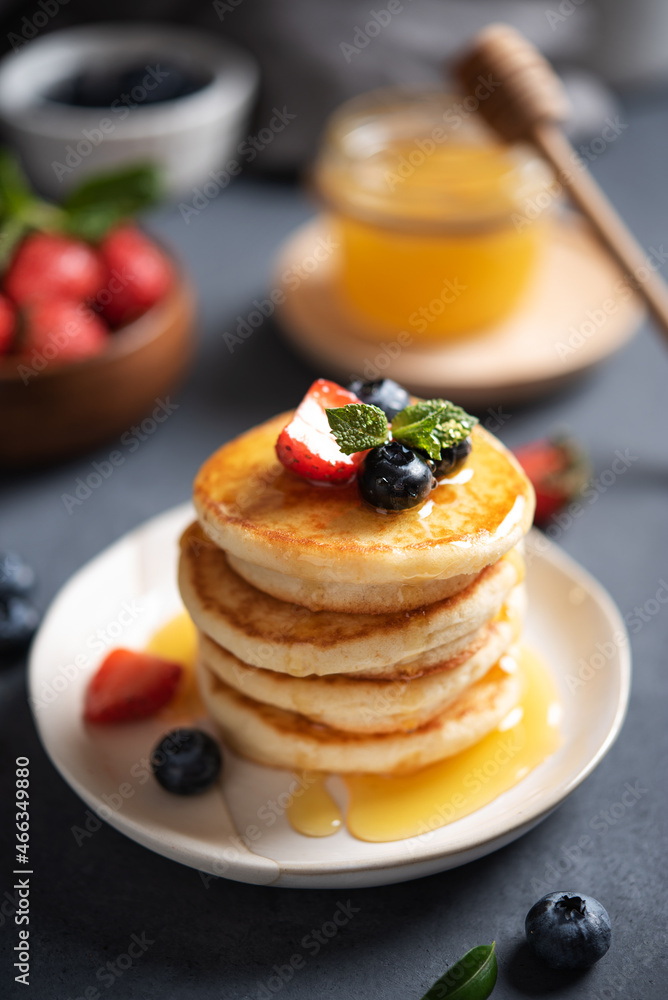 Homemade classic American pancakes in a stack with fresh berries and honey close-up on a blurry dark gray background. The concept of a healthy, delicious and nutritious breakfast. Vertical orientation Homemade classic American pancakes in a stack with fresh berries and honey close-up on a blurry dark gray background. The concept of a healthy, delicious and nutritious breakfast. Vertical orientation