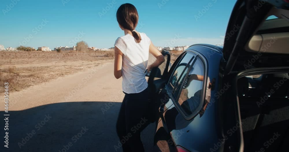 Young beautiful woman has flat tire accident on country road she's is getting out from the car get in the trunk assemble and puts warning triangle