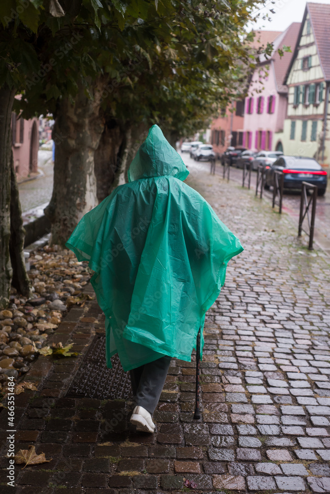 Portrait on back view of woman wearing a green rain coat poncho in the street - obrazy, fototapety, plakaty 