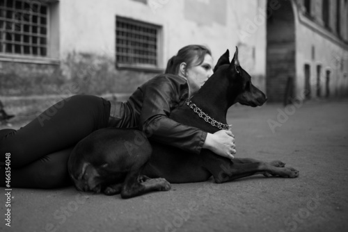 A girl in leather, with a Doberman, in an old yard. photo