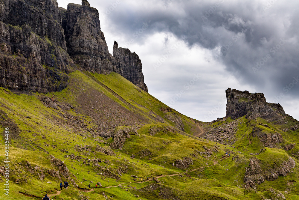 Hikers on a spectacular remote, rocky landscape with a low, moody sky (Quiraing, Isle of Skye)
