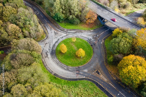 Aerial view of a small traffic roundabout surrounded by colourful trees displaying autumn colours