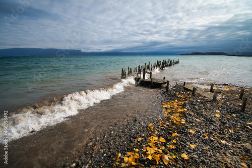 Waves hit hard on the shore  and scatter the remnants of ancient wharf. The horizon can be seen in the distance.