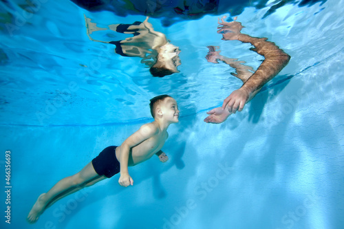 A child, a smiling little boy, swims towards his father's arms underwater in the children's pool. Healthy lifestyle. Swimming training. Concept. Horizontal orientation.