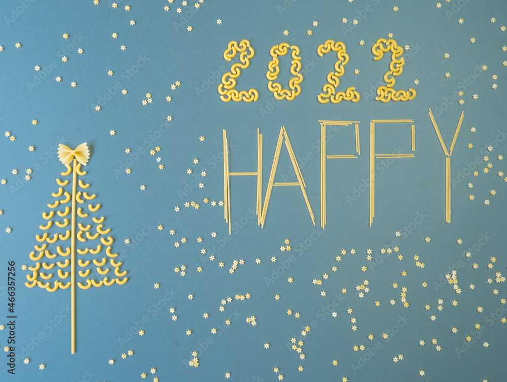 Naklejka premium Christmas tree lined with dry pasta and numbers 2022 and stars from pasta on a blue paper background.