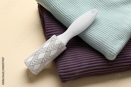 Lint roller with knitted clothes on beige background