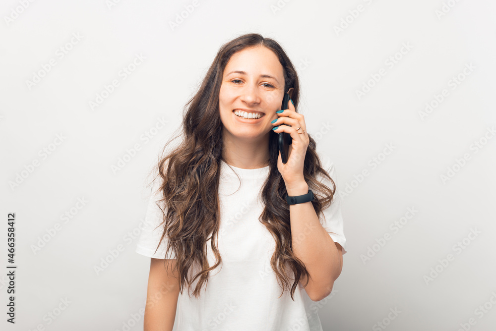Modern young lady is talking over the phone while smiling at the camera. Modern young lady is talking over the phone while smiling at the camera.