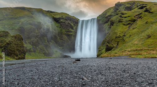 Closeup of Skogafoss waterfall in Iceland at sunrise.  Black and gray gravel in foreground. Green cliffs  no people.