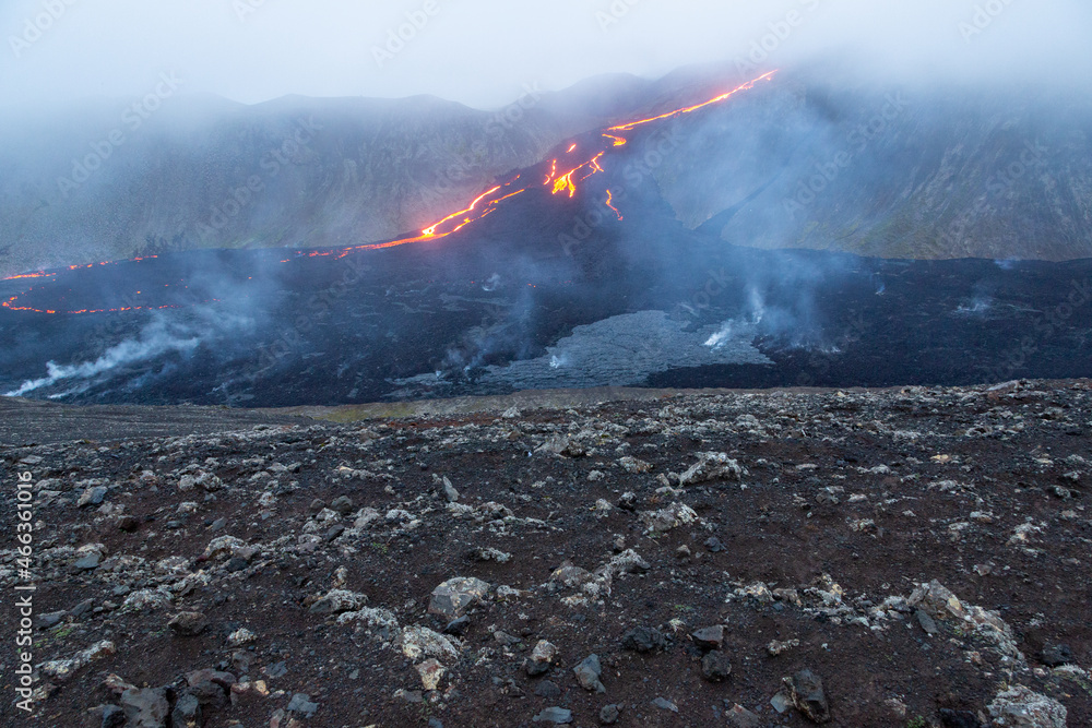 Obraz premium Lava flow from the Fagradsfjall volcano in Iceland. Lava is deep orange color surrounded by dark black lava rock with brown lava rocks in foreground. Steam rising from the ground.