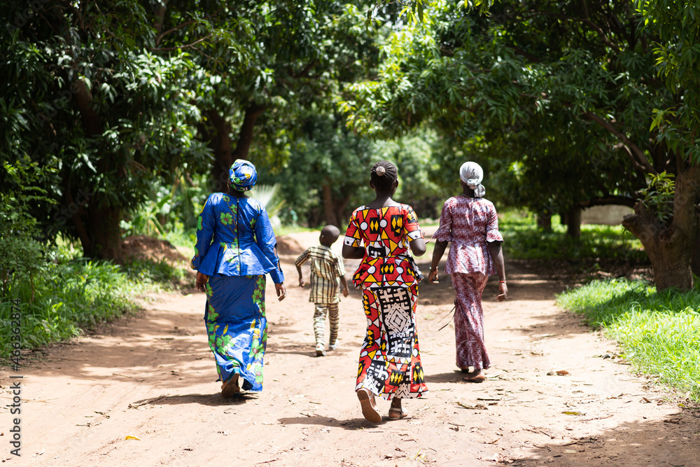 Group of black African villagers strolling along a dirt road among tropical trees - obrazy, fototapety, plakaty 