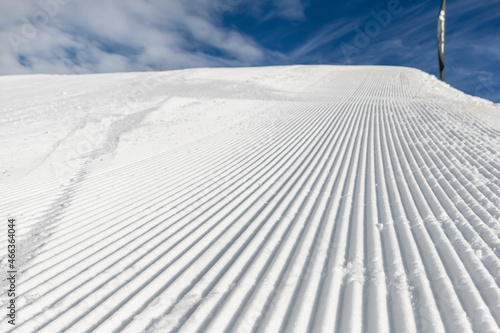 Φωτογραφία Close-up straight line rows of freshly prepared groomed ski slope piste with bright shining sun and clear blue sky background