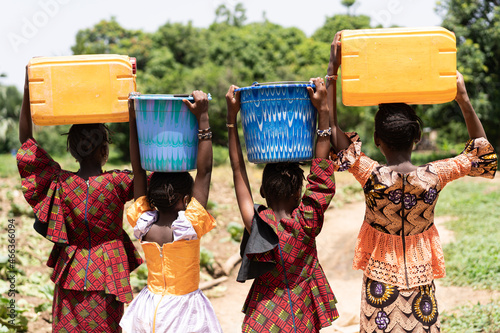 Close up rear view of black African girls carrying heavy water containers on their heads; child labour concept