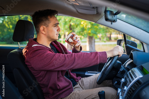Side view of young caucasian man having a cup of takeaway coffee drinking while driving or waiting in car copy space