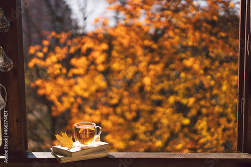 A cup of hot tea and open book on a vintage windowsill. Still life details in home on a wooden window. Read and rest. Cozy autumn concept.