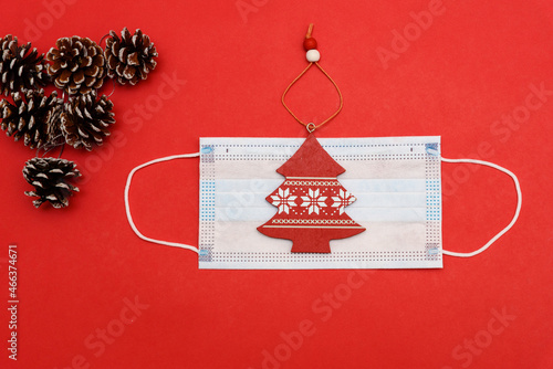 A medical mask with red New Year tree on red background with cones in the upper left corner. Top view with copy space, space for text. Happy New Year 2022 concept.