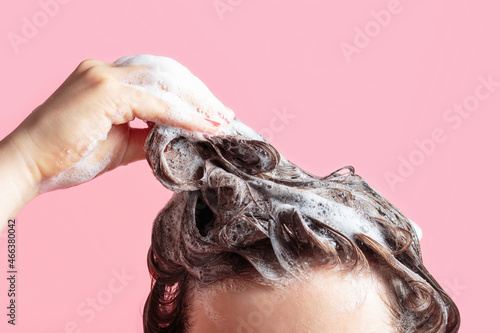 A girl washes her hair with shampoo on pink background, front view. photo