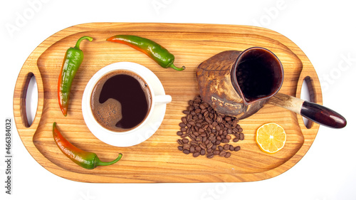 Freshly brewed hot black coffee in a white cup on a wooden board next to a ceramic turkey with coffee beans. hot pepper and lemon