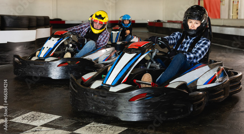 Young positive people in helmets driving racing cars in karting club