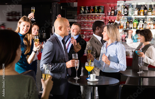 Glad positive middle aged woman with male colleague enjoying office party in bar, talking and toasting with drinks