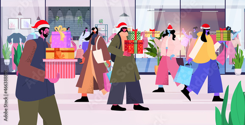 people in santa hats with gifts and shopping bags preparing for christmas new year sale holidays celebration concept