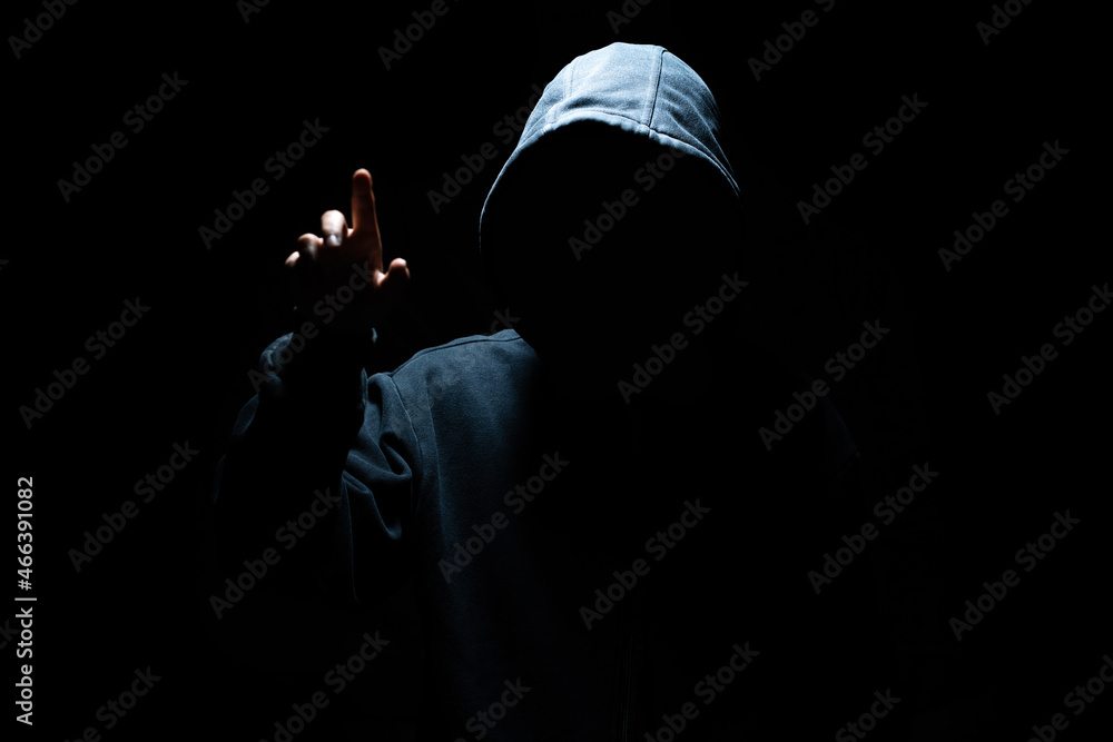 Hacker in mask working with virtual screen against dark background. Concept of cyber security and attack Hacker in mask working with virtual screen against dark background. Concept of cyber security and attack