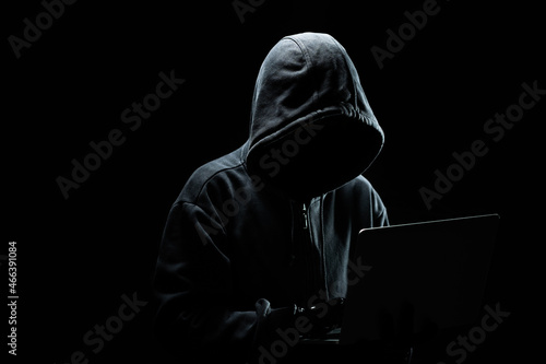 Hacker without a face in a hood on with laptop in the dark