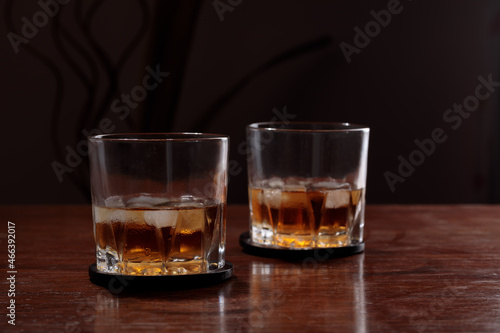 two glasses of whiskey with ice on a wooden table. Dark background with copy space for text.
