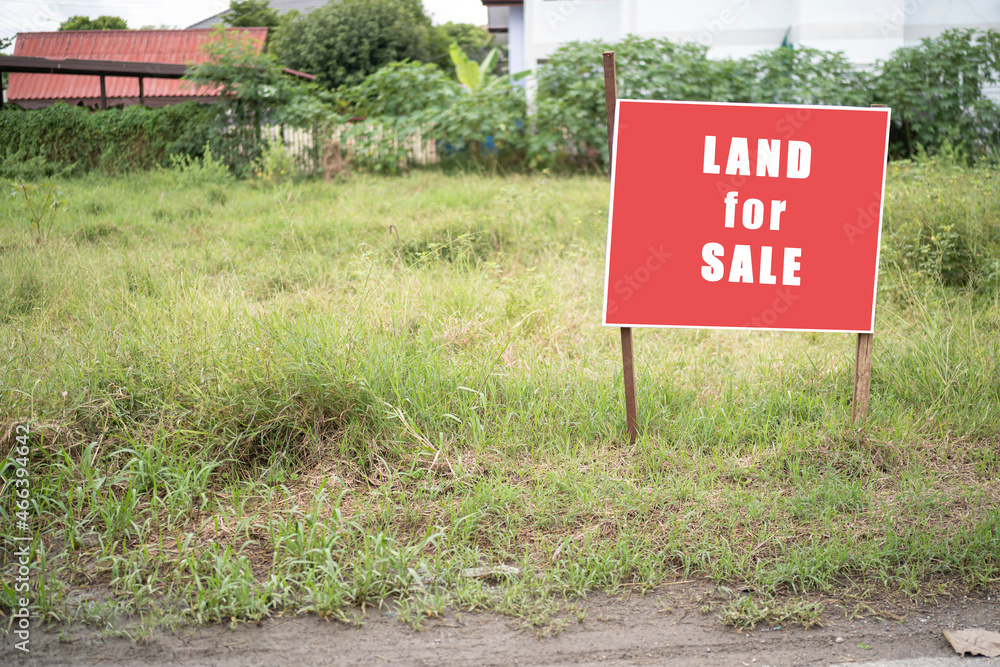 Land for sale sign. Red sign for sale plot. Green lawn behind sign