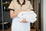maid with white linen and towels in her hands, blonde female enjoy working in hotel, in room
