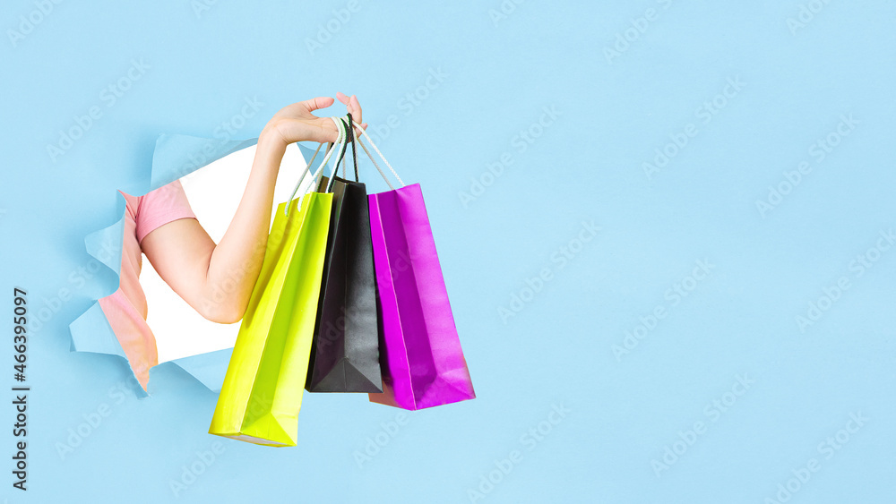 female hand holding shopping bags blue background Break through the torn blue wall.season sale and shopping .