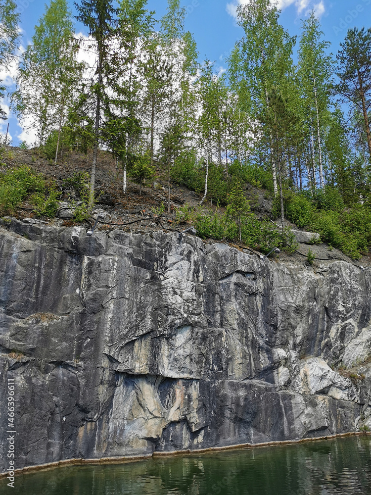 View from the water on the steep slope of the flooded Marble Canyon, where trees grow, in the mountain park Ruskeala on a sunny summer day.