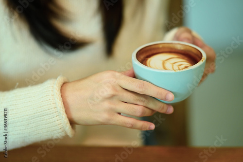 Close up view young woman in white sweater holding cup of hot coffee.