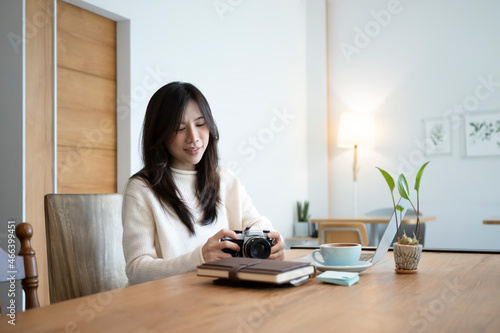 Smiling female freelancer holding camera and working with laptop.