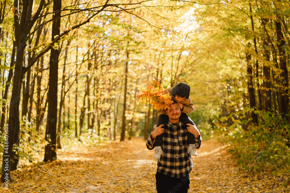 Fototapeta premium Happy young dad and son are walking in the autumn forest. Autumn outdoor activity for family with kids. Happy father's day. Family day. Autumn day. Happy family leisure.