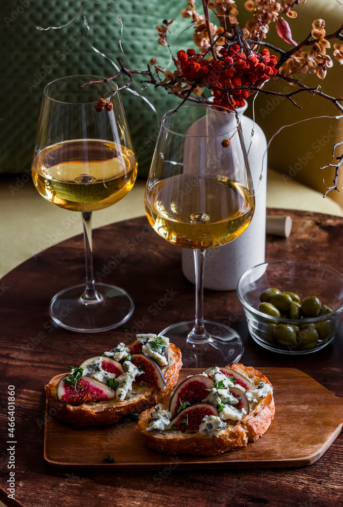 Two glasses of white wine and gorgonzola bruschetta figs in a cozy interior on a wooden table